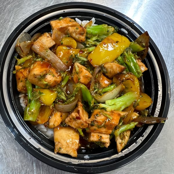 Chicken and vegetable stir-fry with broccoli, peppers, and onions over rice in a black bowl.