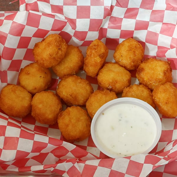 Golden-brown fried cheese curds with a side of ranch dressing in a red and white checkered basket.