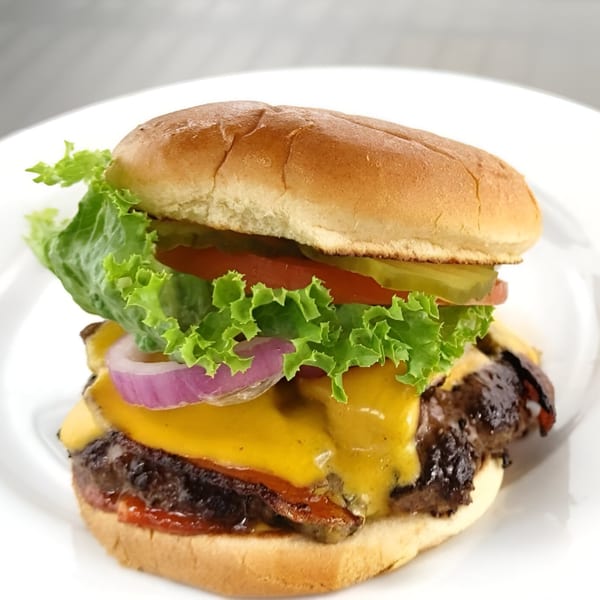 A Busta's Burger with melted cheese, lettuce, tomato, pickles, and red onion on a white plate.