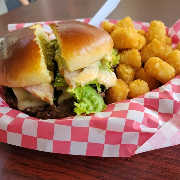 A Busta's Burger cut in half, with melted cheese, lettuce, and sauce, served with tater tots.