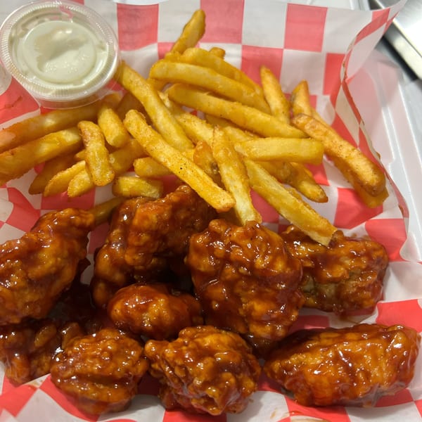 Busta's Burgers boneless wings coated in sauce, with a side of golden fries and dipping sauce.